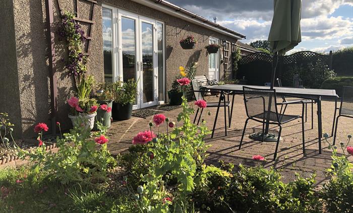 Front view of Blackthorn Lodge showing the lounge patio doors, front door and patio garden area with garden furniture including a table, 4 chairs, par